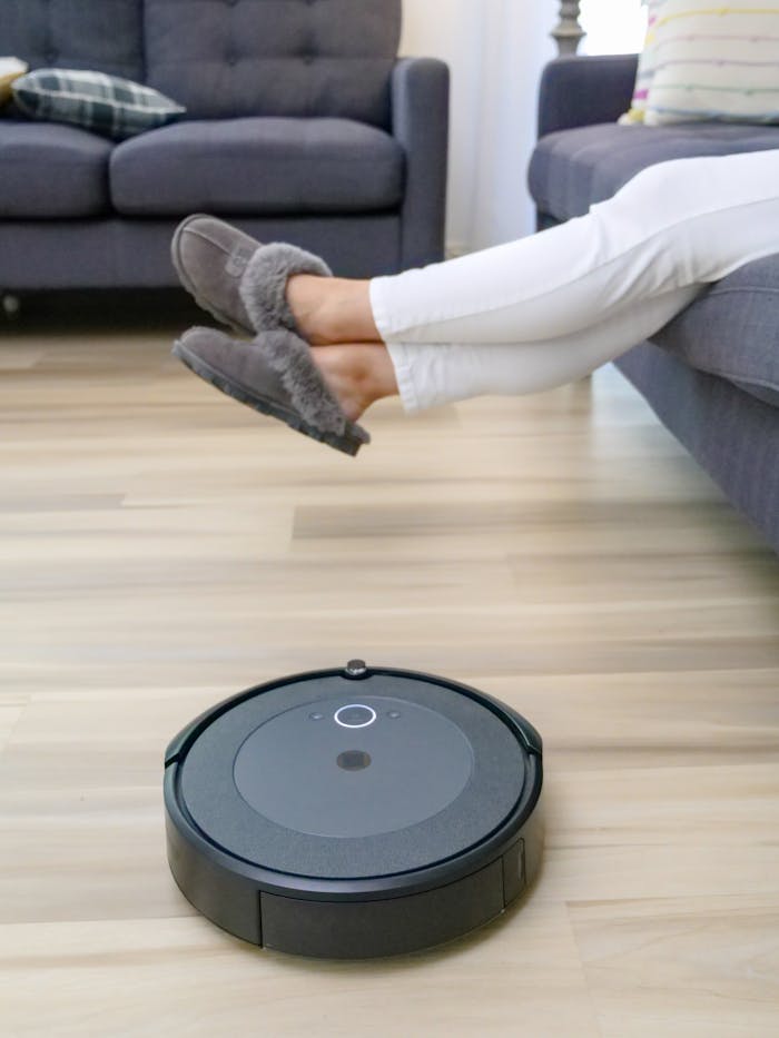 Home Autonomous robot vacuum cleaning hardwood floors under relaxing person's feet.